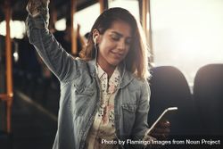Woman listening to earbuds while standing on bus 0WrDMb