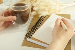 Woman writing in notebook with cup of coffee