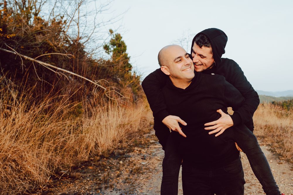 Smiling man holding on back cheerful guy on road on hill