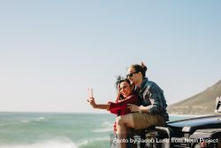 Woman taking selfie with her boyfriend at the beach on a road trip 0KEOy4