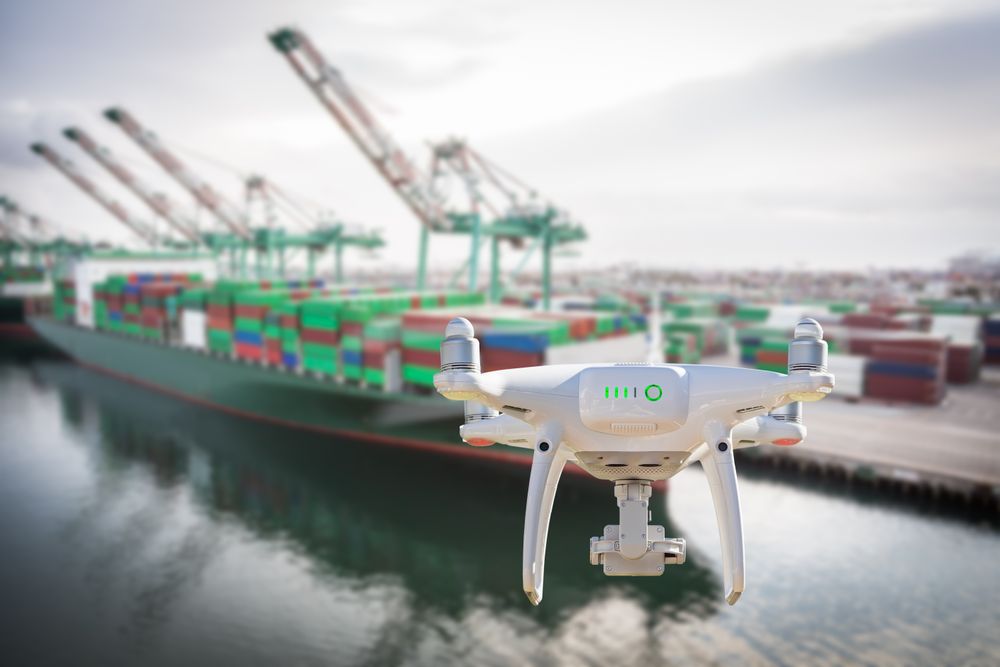Unmanned Aircraft System Quadcopter Drone In The Air Near Large Shipping Vessel and Dock with Crates