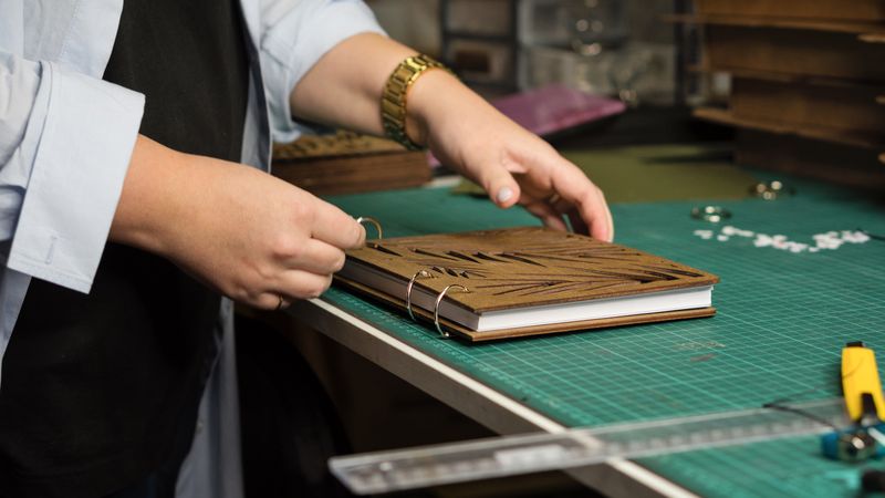 Female hands hold notebook with removable blocks and wooden cover together in workshop
