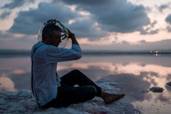 Man with fish tank on head sitting at seashore