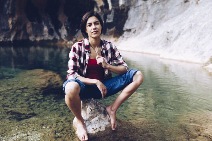 Cheerful woman sitting on rock in clear water