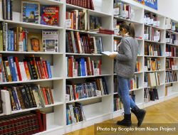 Young woman in jeans standing beside bookshelves at the library 476ok5