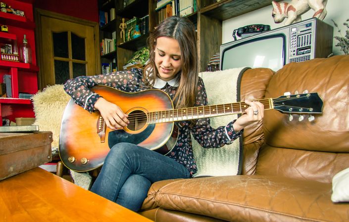 Young hipster woman playing acoustic guitar at home