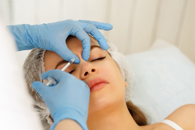 Cosmetologist at med spa injecting botox between eyes in female client