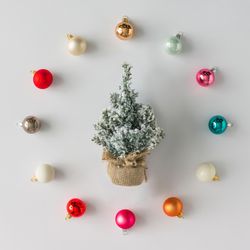 Circular border of colorful Christmas bauble decorations on light background with miniature tree