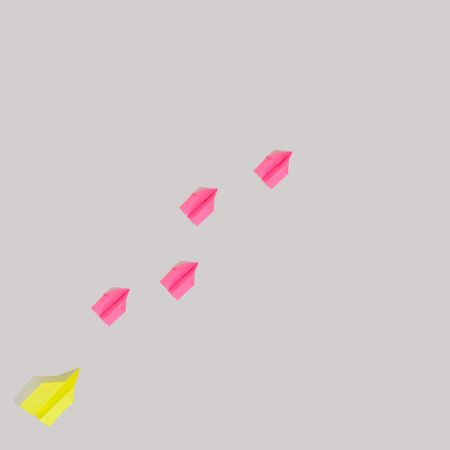 Flat lay of paper airplanes flying diagonally in pink and yellow flying up
