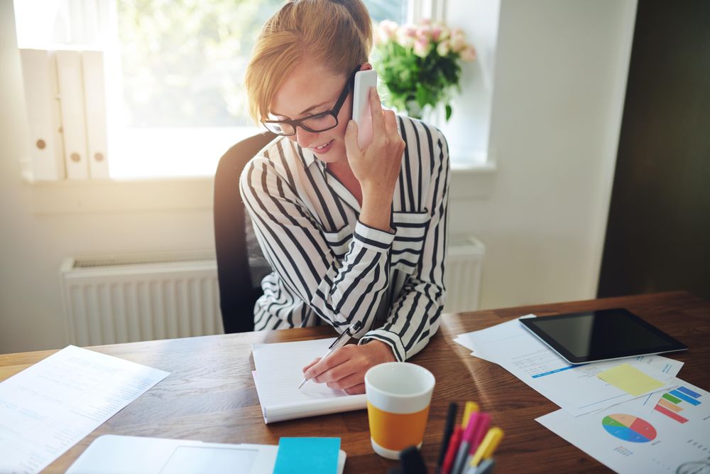 Woman in striped shirt taking phone in home office with coffee