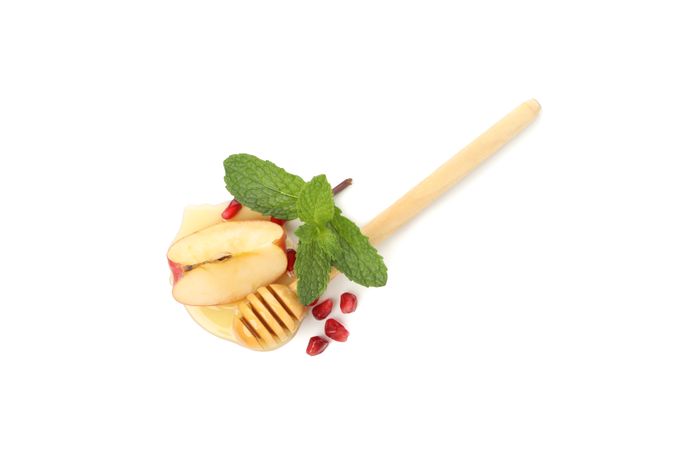 Top view of honey dipper with mint leaves, pomegranate seeds, and an apple quarter