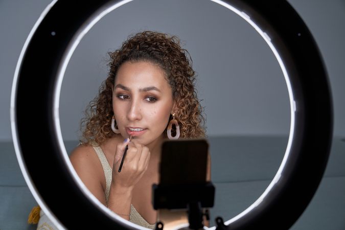 Charming woman applying lipstick with brush while recording vide
