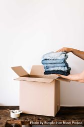 Cropped image of person holding stack of folded t-shirt beside cardboard box 4OXzgb