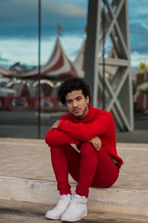 Man in red shirt sitting on sidewalk