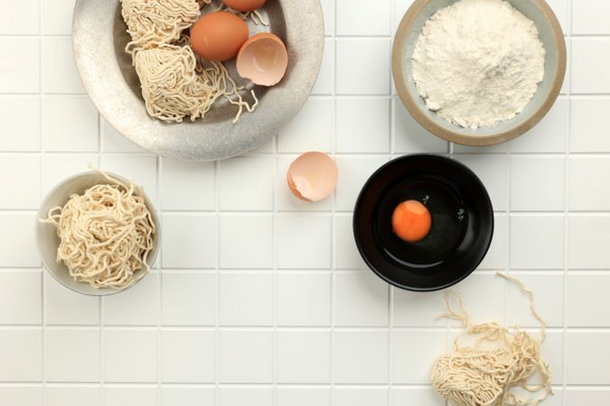 Top view of eggs, flour and noodles on tiles
