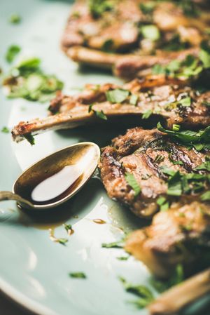Plate of grilled lamb chops with parsley garnish on light blue plate, vertical composition, close up