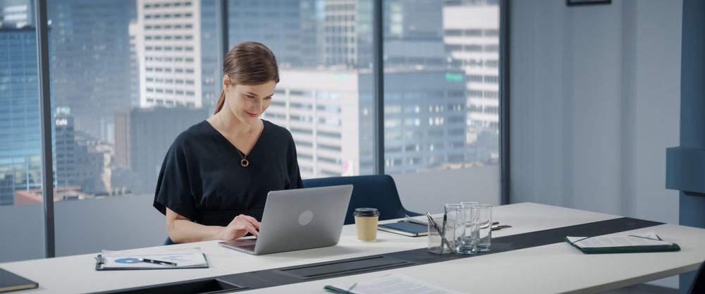 Portrait of Successful Businesswoman Working on Laptop Computer in Her Big City Corner Office.