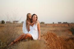 Adult female and child in summer dress relaxing on top of cliff at dusk