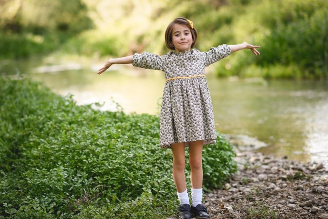 Girl in dress standing by river with her arms open