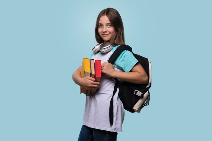 Smiling girl holding books and wearing backpack, preparing for school