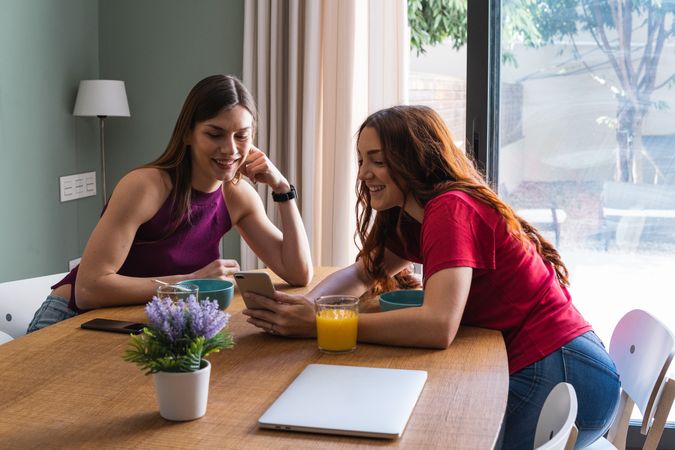 Happy women having lunch and browsing smartphone at home