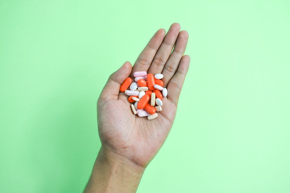 Variety of colorful medication and vitamins in hand above green table