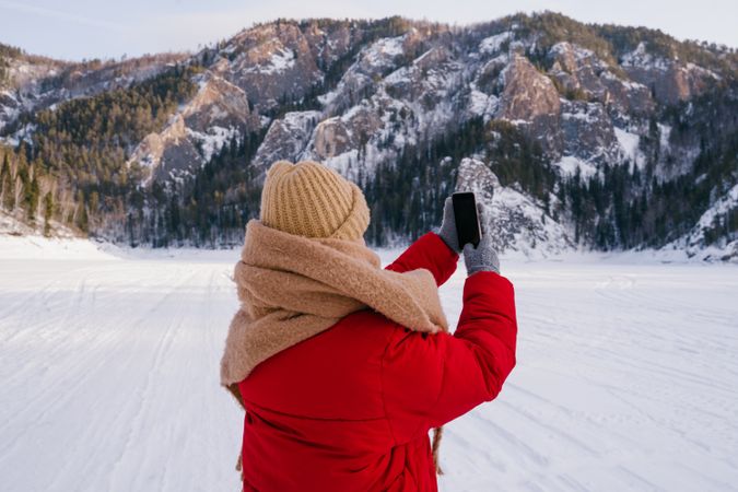 Woman taking picture of snowy mountains with smartphone