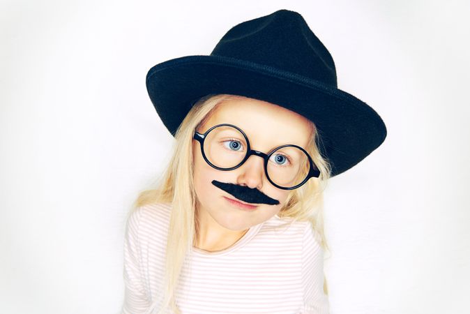 Serious blonde girl wearing fake mustache, hat and glasses