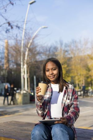 Female in plaid shirt sitting outside with tablet and coffee