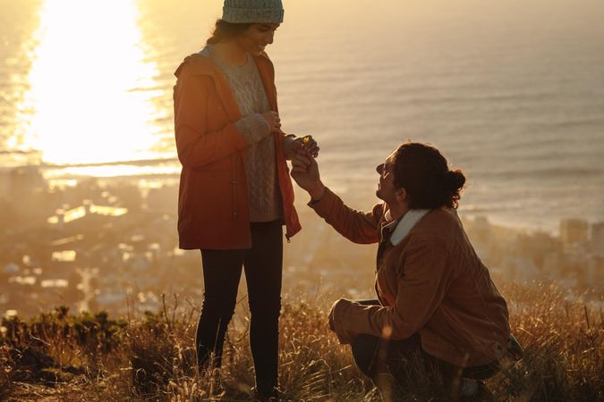Man making marriage proposal to his girlfriend on the mountain peak at sunset
