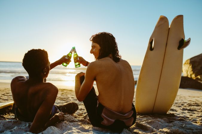 Rear view of two young surfers toasting beers on ocean beach
