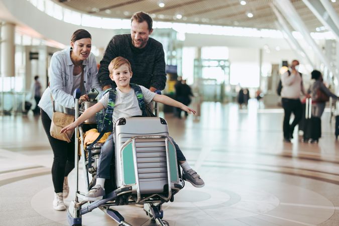 Parents moving luggage trolley with their son at airport