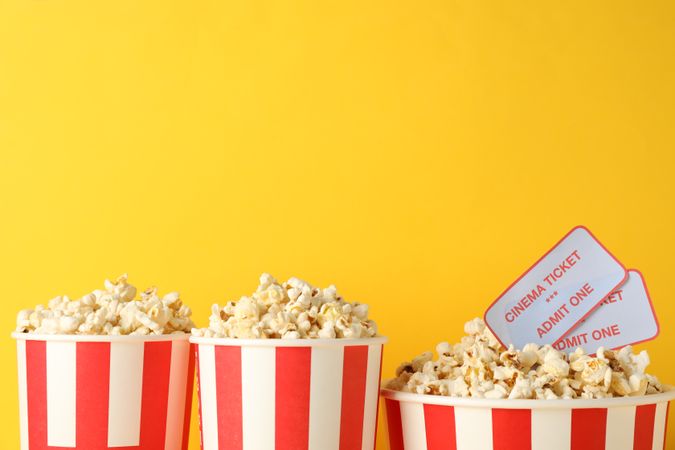 Striped buckets with popcorn on yellow background, copy space