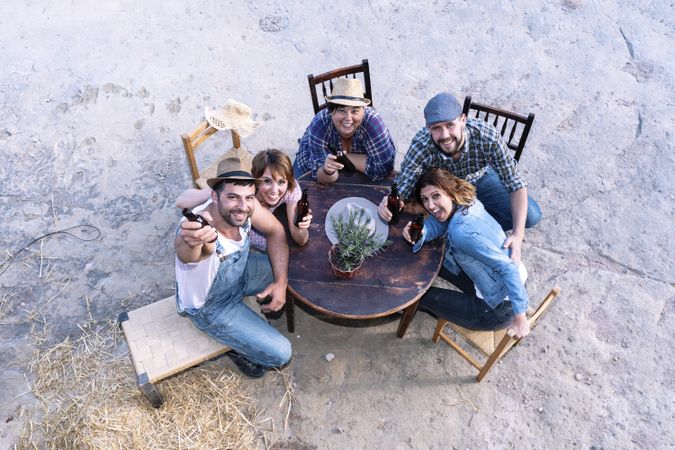 Aerial view of a group of friends sitting around a table holding beers