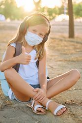 Girl in mask sitting on ground and showing thumb up