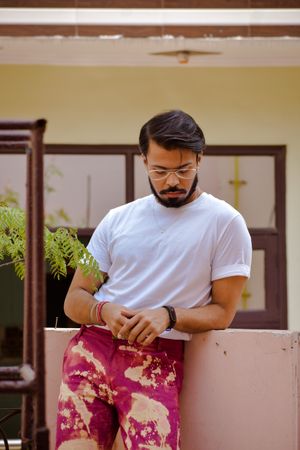 Bearded man in light shirt and purple pants leaning on balustrade outdoor