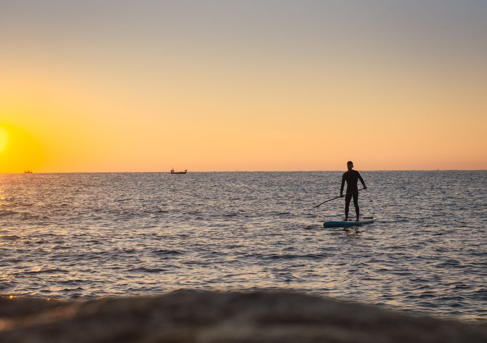 Man practicing paddle surfing with neoprene in a sunrise