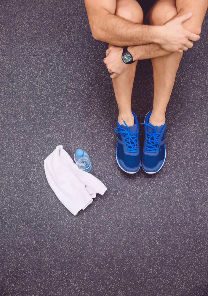 Legs of person sitting on gym floor with towel and water bottle