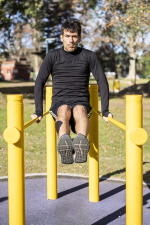 Front view of a young man doing abdominal exercises on a public equipment in outdoor fitness