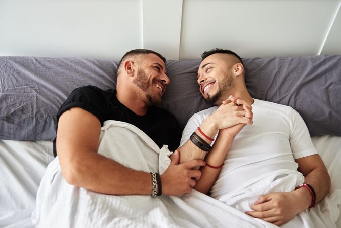 Smiling gay couple hugging on bed