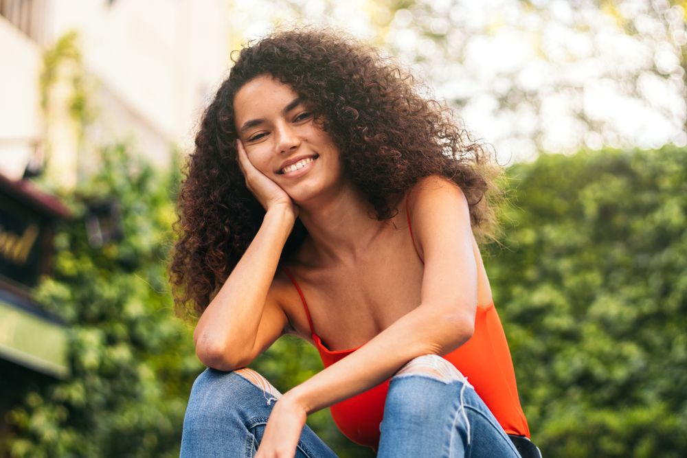 smiling young woman with curly hair portrait sitting on a stairs