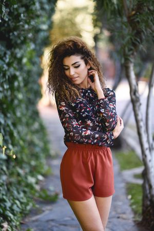 Arab woman looking down wearing casual clothes in the street lined with greenery