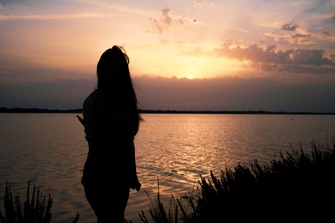 Silhouette of woman standing by the water at sunset