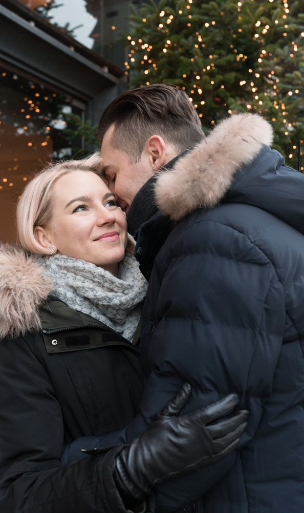 Smiling couple having fun on street near fir tree with fairy lights