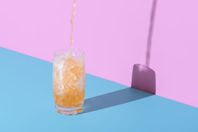 Ice tea with crushed ice in a glass, minimalist on a pink and blue background