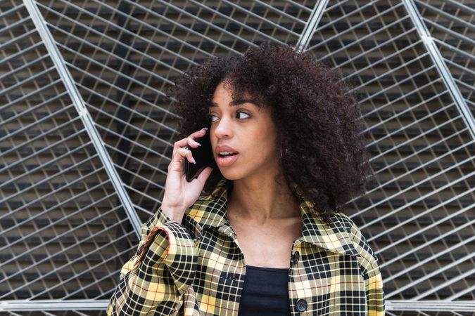 Trendy woman talking on smartphone against grid fence
