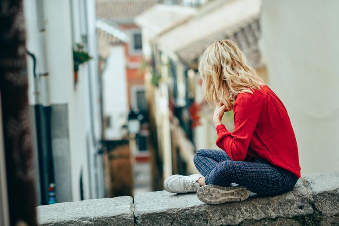 Side of blond woman sitting on stone wall with legs crossed
