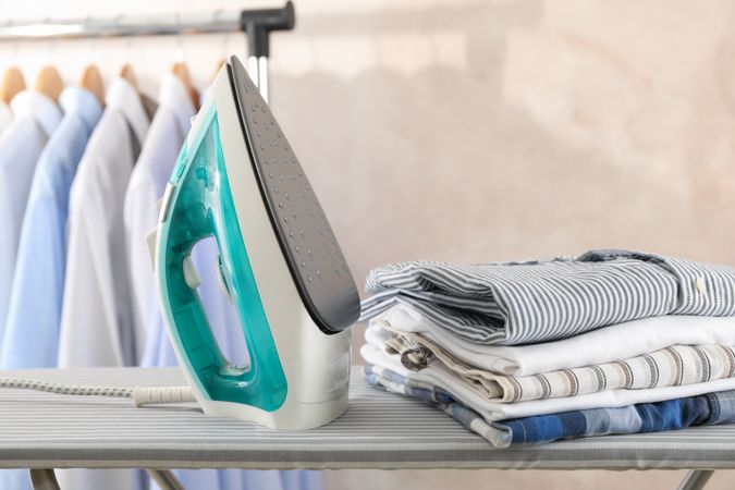 Iron and stack of t-shirts on ironing board, space for text