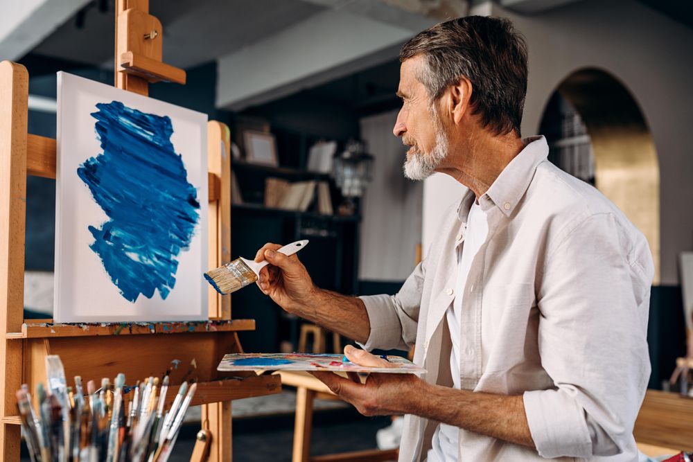 Older male artist with large brush at his easel