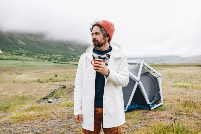 Male waking up from tent with ceramic mug on overcast day